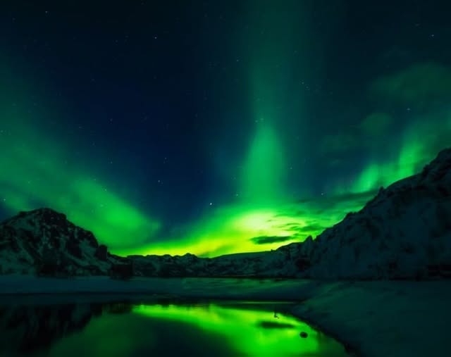 Aurora borealis over snowy mountains reflected in a still lake