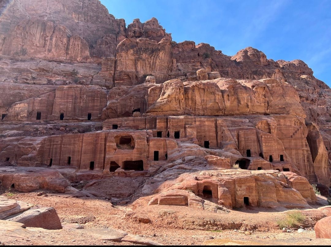 Rows of ancient Nabataean tomb doorways carved into towering rose-red sandstone cliffs at Petra, Jordan