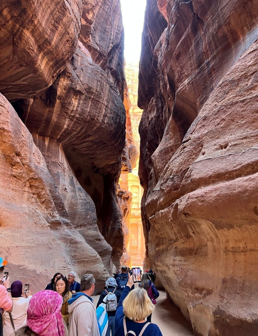 Tourists walking through the Siq canyon passage into Petra with the Treasury visible at the end