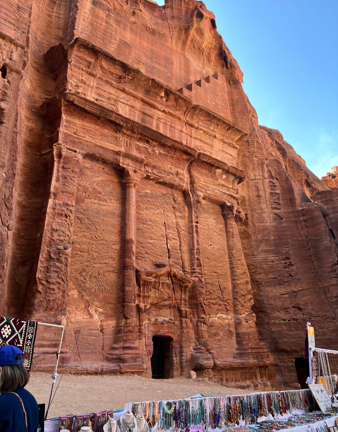 Carved Nabataean tomb facade at Petra with a colorful souvenir and jewelry market in front