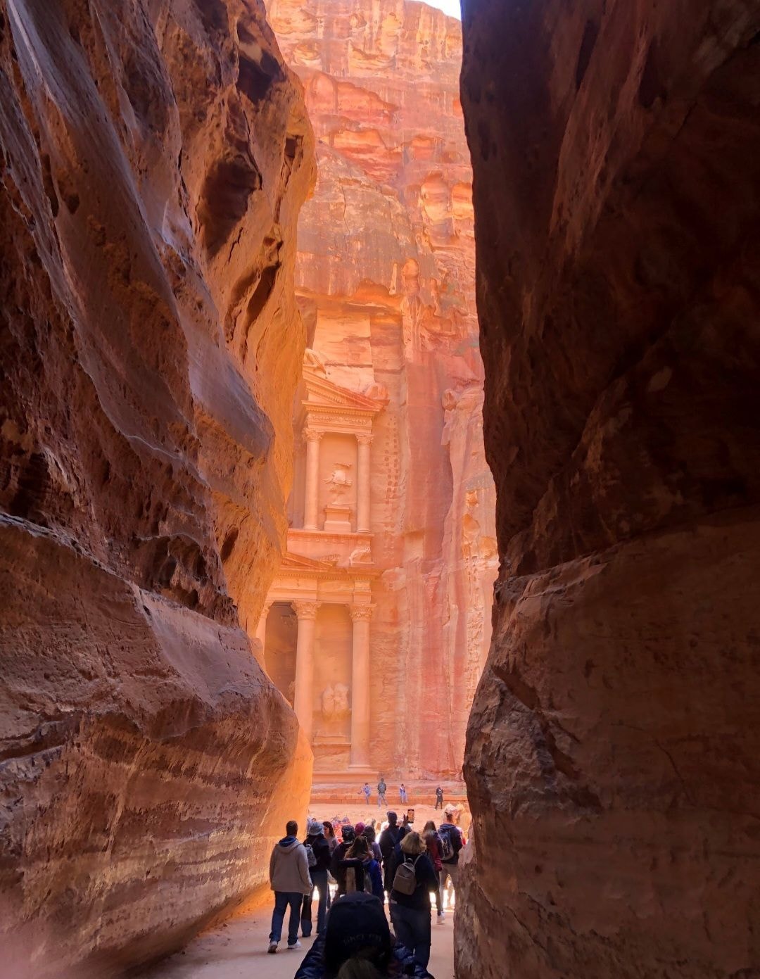 Tourists walking through the narrow Siq canyon with Petra's Treasury visible at the end framed by towering sandstone walls