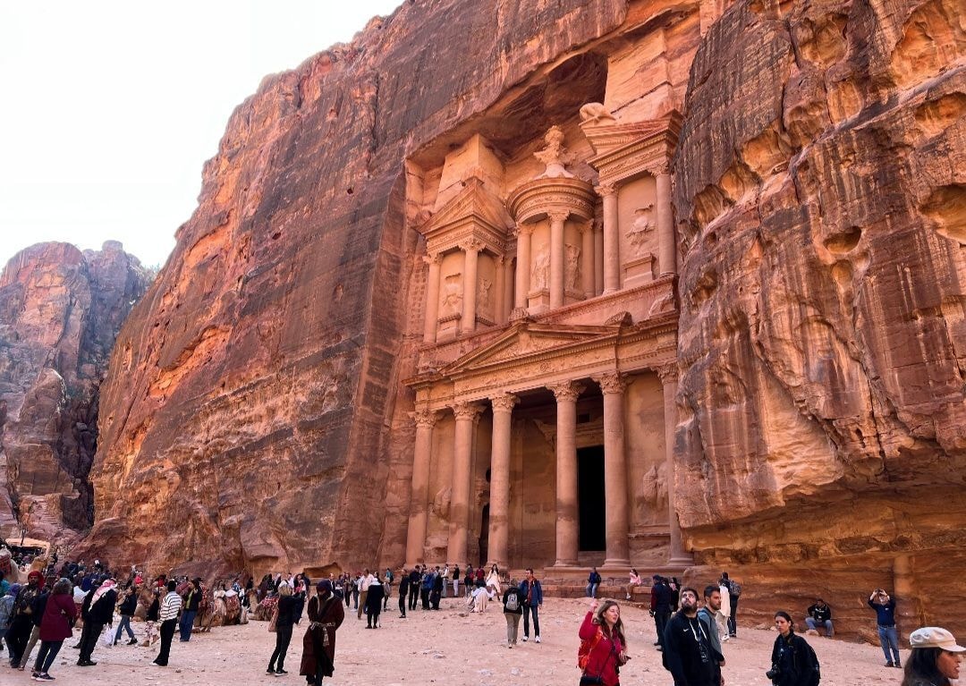Crowds of tourists gathered in front of the Treasury at Petra, carved into the rose-red sandstone cliffs of Jordan