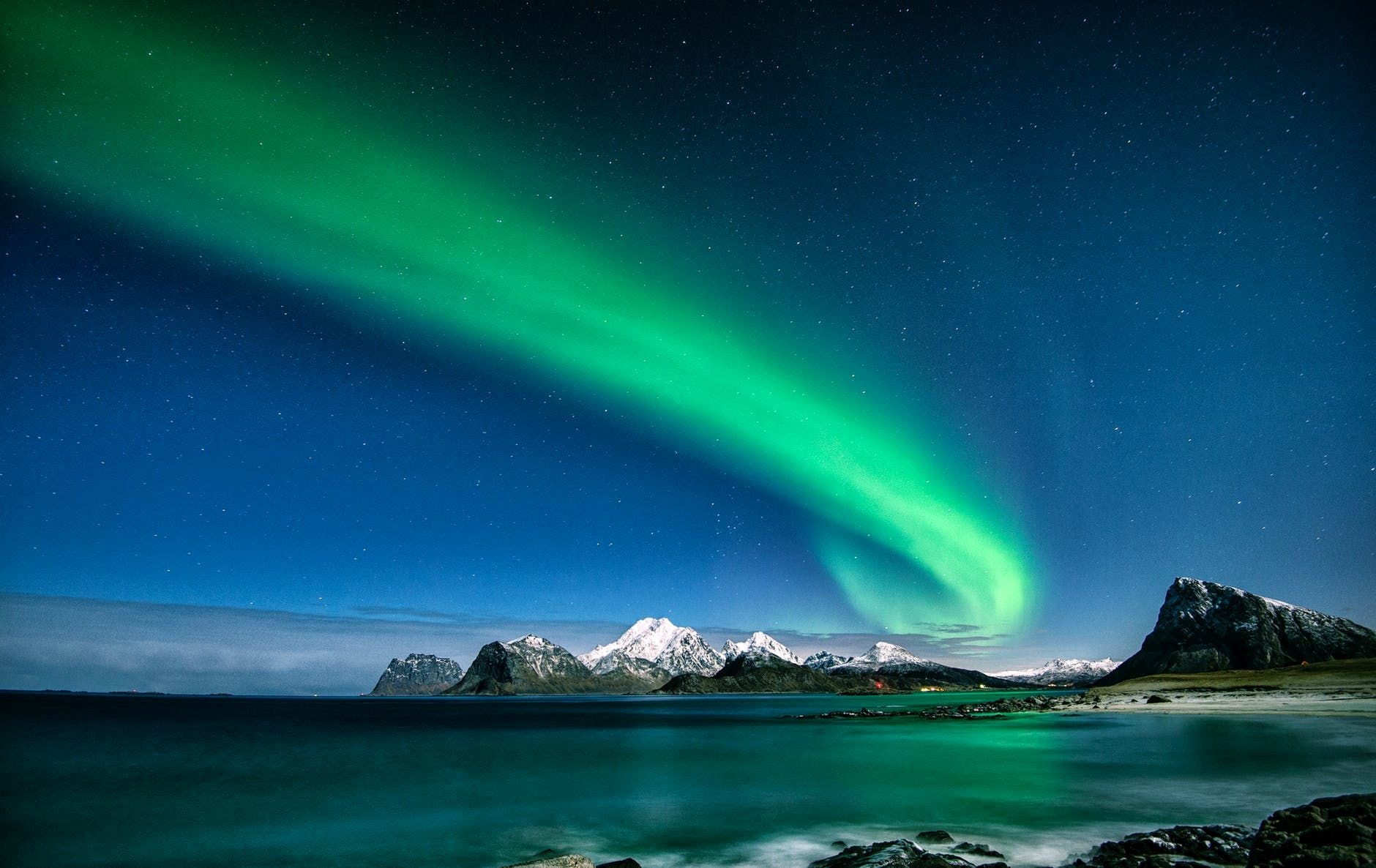 Brilliant green aurora borealis sweeping over snow-capped mountains and a calm arctic sea
