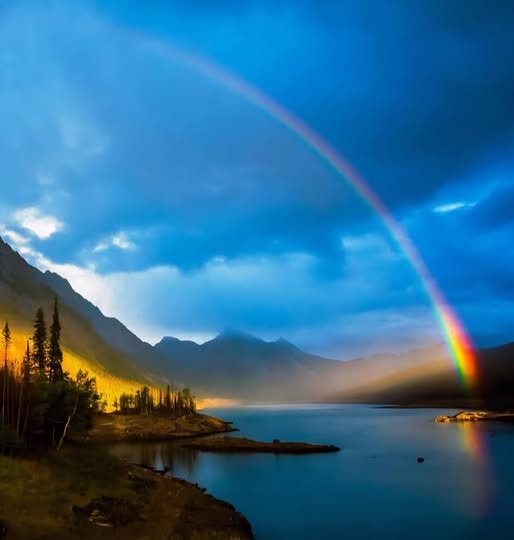 Rainbow over a mountain lake beneath a dramatic blue sky